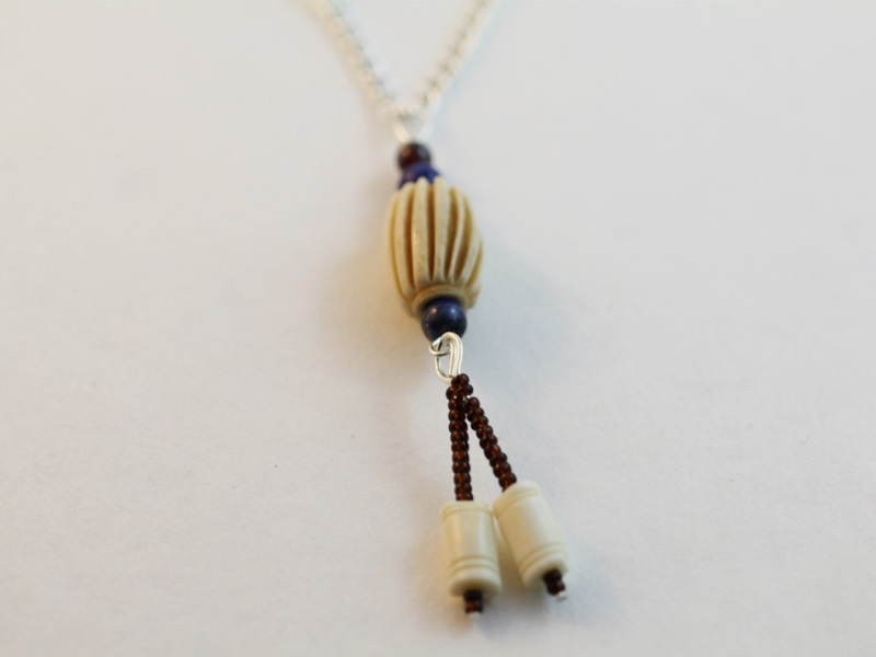 A necklace pendant made with bone feature beads, lapis lazuli beads, garnet beads and dark red seed beads.