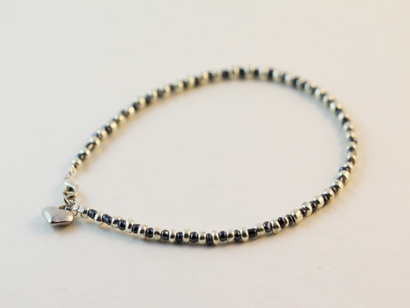 A metallic beaded anklet with a silver colored heart shaped charm