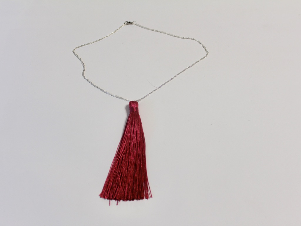 A silver chain necklace with a hot pink tassel pendant